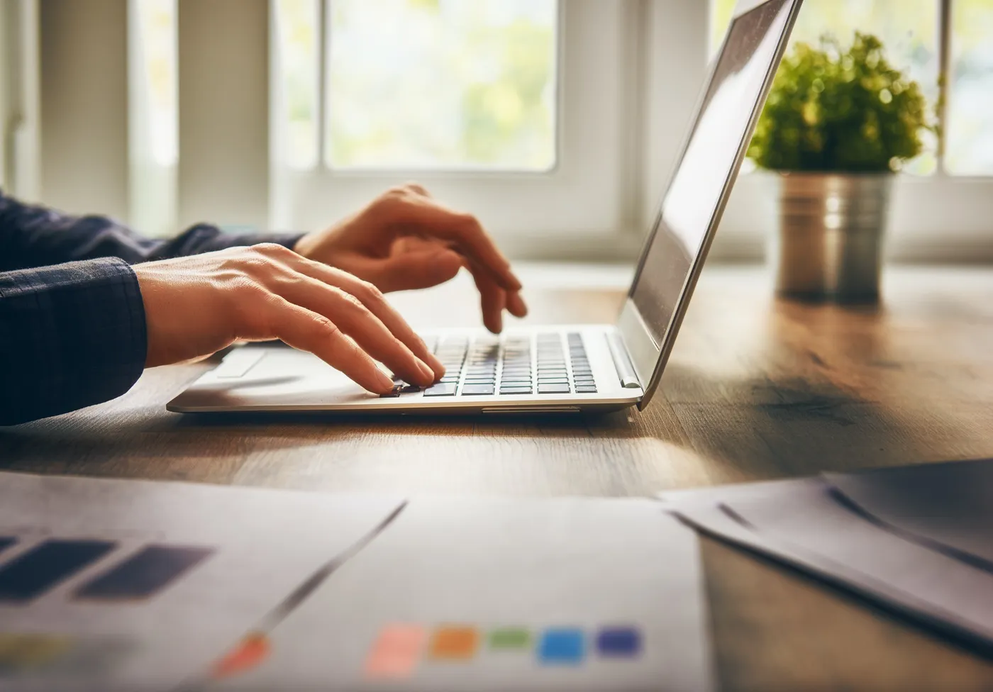 Hands typing on a laptop beside printed reports