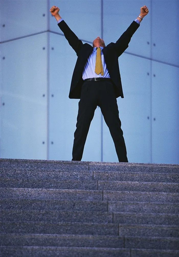 A businessman on stone steps with arms raised